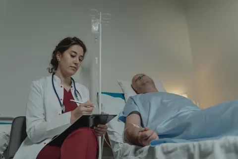A clinician reviewing a chart beside a hospital bed