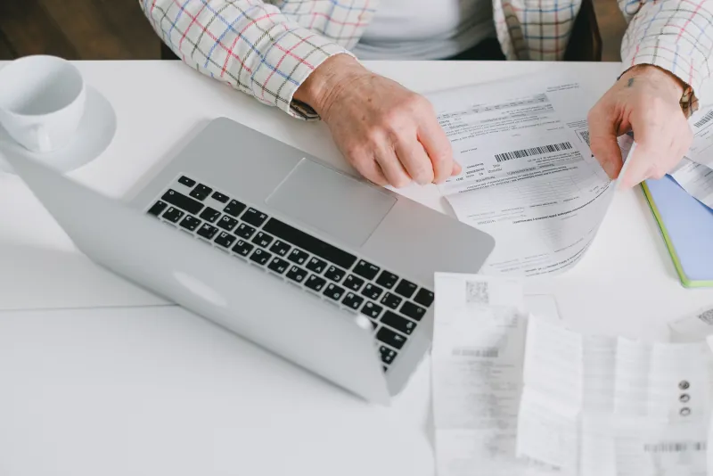 Hands organizing paperwork beside a laptop