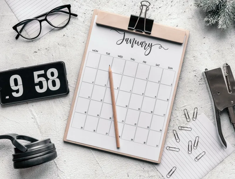 A paper planner, pencil and glasses on a desk